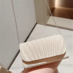 Cremefarbene Clutch mit gerafftem Klappenverschluss und dünner Silberkette auf einem Bein