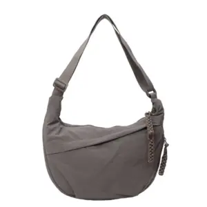 Graue Schultertasche aus Stoff mit Verstellriemen und geflochtenem Anhänger auf weißem Hintergrund