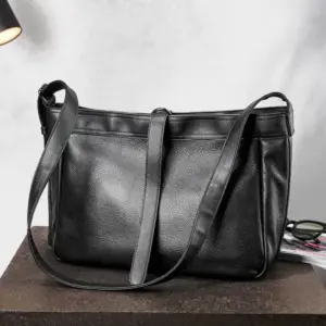 Schwarze große Umhängetasche aus Leder mit Gurten und Reißverschluss auf einem Holztisch