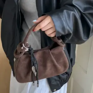 Braune Handtasche in Wildleder-Optik mit Kordel und Herzanhänger, in der Hand getragen