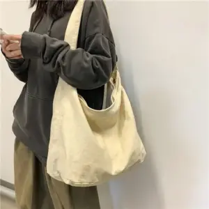 Cremefarbene Hobo-Tasche aus Stoff, quer getragen von einer Person in dunkler Kleidung