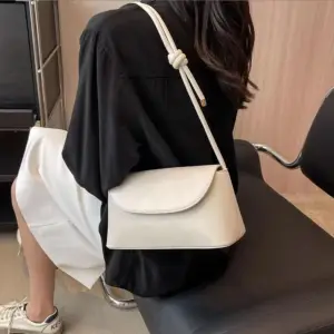 Cremeweiße Schultertasche mit Klappe und geknotetem Riemen, von hinten auf der Schulter getragen
