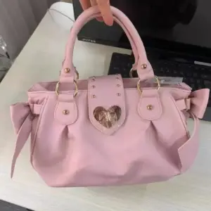 Rosa Handtasche mit Schleifen an den Seiten und Herzverschluss, in der Hand gehalten