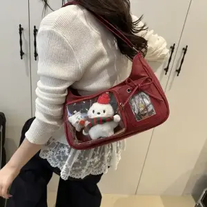 Rote Schultertasche mit transparenten Fächern und Plüschfigur, auf der Schulter einer Person getragen