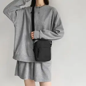 Kleine schwarze Umhängetasche, von einer Person zu grauem Pullover getragen